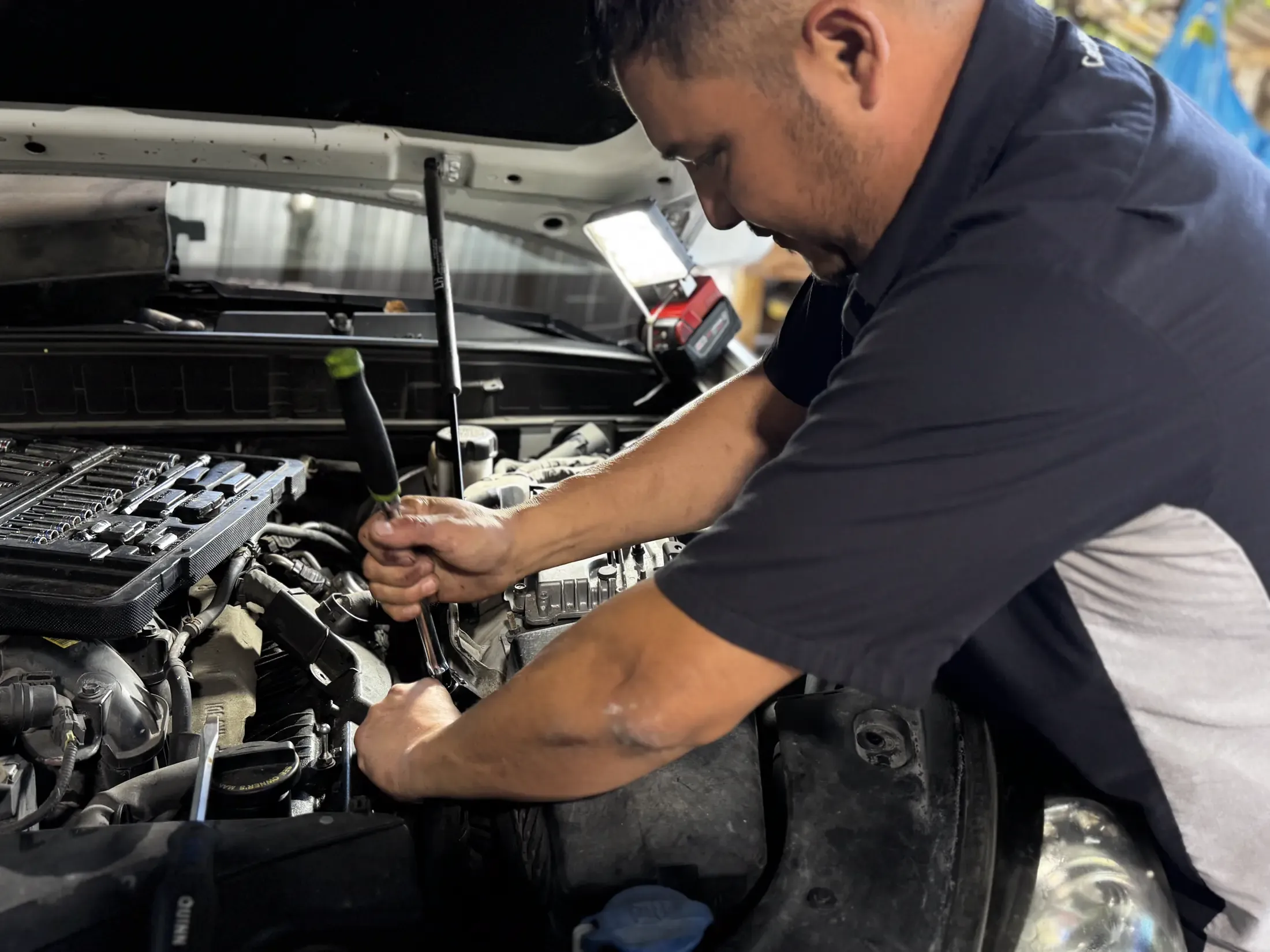 Technician working on an engine under a raised hood outdoors